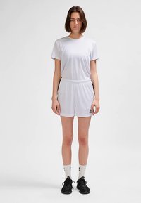 Ensemble de t-shirt et short de sport blancs, manches courtes, taille élastique, tissu lisse, avec un petit logo sur le short, accompagné de chaussures noires.