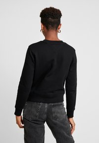 Musta collegepaita, jossa on pyöreä kaula-aukko ja ribbauskudot hihansuissa. Valmistettu pehmeästä materiaalista, jossa on sileä pinta ja yksinkertainen, siisti muotoilu.