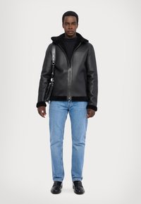 Veste en cuir noir avec un col en peluche, fermeture éclair et poches latérales, assortie à un jean bleu clair et des chaussures noires.