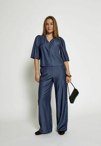 Haut bleu marine à manches courtes avec des détails froncés, associé à un pantalon large bleu marine, présentant une texture lisse et un sac à main noir.