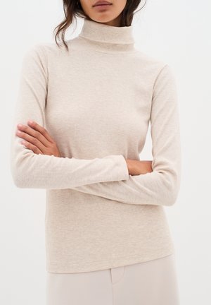 Beige Rippen-Turtleneck Langarmoberteil, weicher Stoff, enganliegendes Design, mit hohem Kragen und dezentem Muster, kombiniert mit hellen Hosen.