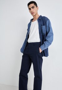 Denim shirt in dark blue, long-sleeved, with a pocket; paired with fitted navy trousers, creating a structured silhouette.