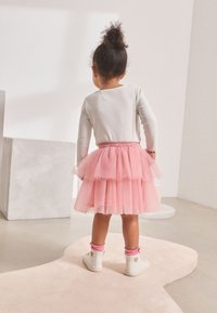 Pink tulle skirt with layered ruffles, featuring a sparkly waistband. Paired with white sneakers and pink ankle socks, viewed from behind.