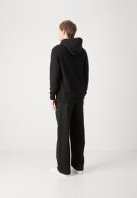 Zwarte hoodie met een capuchon, voorzien van lange mouwen en een ontspannen pasvorm, gecombineerd met zwarte wijde broek en witte sneakers.