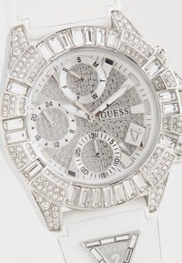 Zilverkleurig horloge met een sprankelende bezel en witte siliconen strap. Beschikt over drie subdials en een geprofileerde wijzerplaat met kristalaccenten.