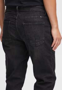 Czarne dżinsy z denimu o luźnym kroju. Posiadają dwie tylne kieszenie, subtelne przeszycia i średni stan. Materiał ma gładką teksturę.