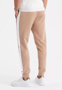 Slim-fit beige sweatpants met witte zijkanten, gemaakt van gladde stof, met een elastische tailleband en boorden, gecombineerd met witte sneaks.