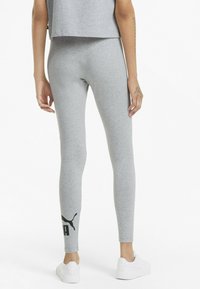 Leggings grises hechos de un material suave con un diseño ajustado. Presentan un logo negro de Puma en la pierna izquierda y se llevan con zapatillas blancas.