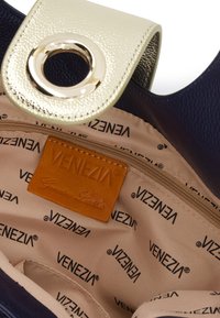 Indvendig i den sorte læder håndtaske med beige foring, der har et gentaget "Venezia" mønster. Guldhardware og en cirkulær detalje på klappen.