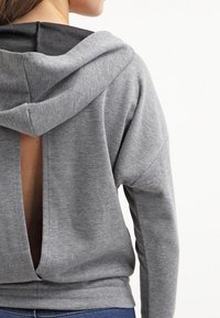 Sudadera gris con un corte en la espalda y una capucha forrada de malla negra. Textura suave, corte relajado y dobladillo acanalado. Sin herrajes visibles.