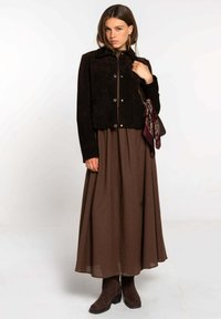 Chaqueta de ante negra con botones a presión, combinada con una larga falda marrón y botines de ante marrones oscuros. Incluye un pañuelo con un diseño como acento.