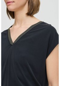 Black V-neck top with short sleeves. Features textured gold stitching along the neckline. Soft, smooth fabric; relaxed fit.