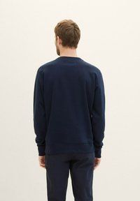 Granatowa bluza z okrągłym dekoltem, z długimi rękawami, o teksturowanej tkaninie oraz ściągaczach przy rękawach i na dole. Tylny widok ukazuje czysty, bezszwowy design.