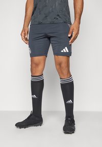 Pantaloni sportivi grigi con logo Adidas bianco, abbinati a calzini neri con strisce bianche e logo. Scarponi da calcio neri con superficie strutturata.