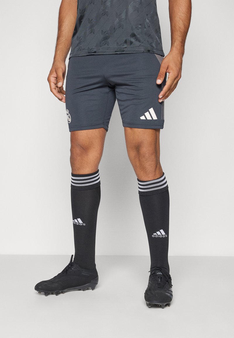 Pantaloni sportivi grigi con logo Adidas bianco, abbinati a calzini neri con strisce bianche e logo. Scarponi da calcio neri con superficie strutturata.