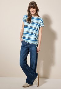 Camiseta de manga corta a rayas en azul claro y marino, combinada con unos vaqueros de pierna ancha en azul oscuro. El calzado son zapatillas de color claro.