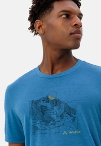 Blauwe T-shirt met een bergafbeelding in zwart en geel, gemaakt van zachte stof. Heeft een ronde hals en korte mouwen.