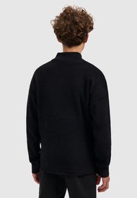 Zwarte gebreide trui met een hoge kraag, een iets oversized pasvorm en ribbelstructuur. Beschikt over lange mouwen en een rechte zoom.