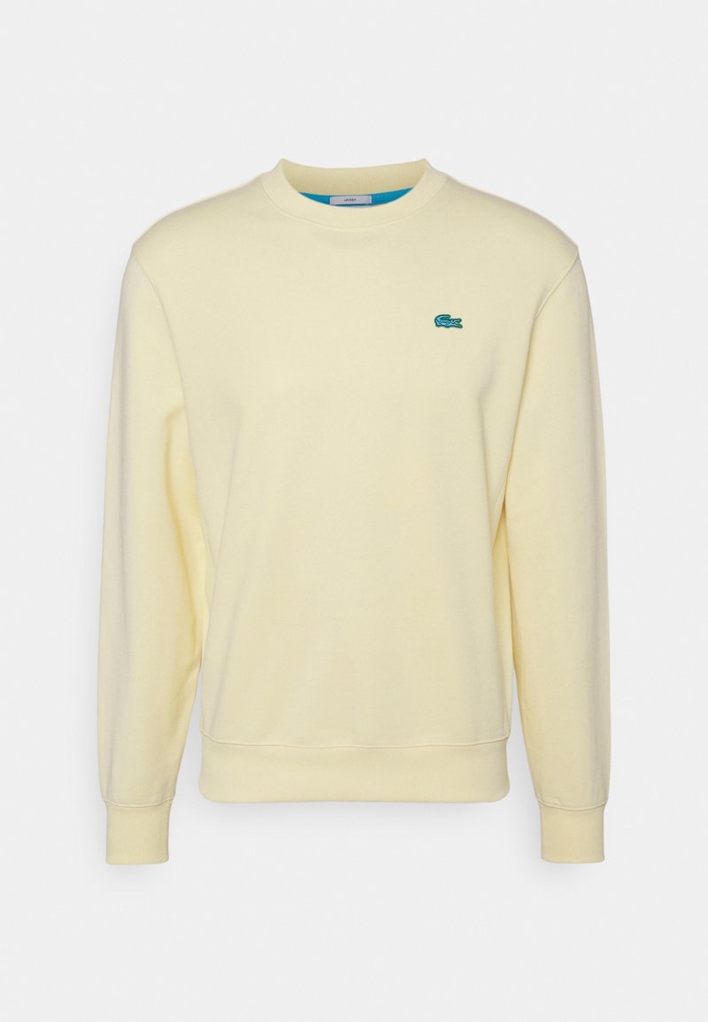Sweat-shirt crème à manches longues avec col rond, poignets et bas côtelés, avec un petit logo crocodile vert sur la poitrine.