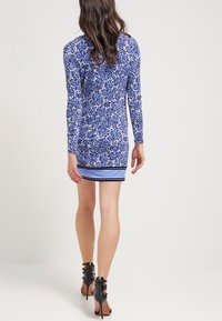 Långärmad klänning med ett blått blommönster och randig nederkant, tillverkad av ett slätt tyg. Svarta högklackade skor fulländar stilen.