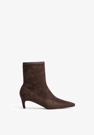 Bruna mockaskinnsankelstövlar med spetsig tå och smal klack. Har en mjuk textur och en högskaftdesign.