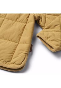 Gequilted bruine jas van een zachte, textuurachtige stof, met afgeronde randen en een label op de naad. De binnenkant toont een contrasterende kleur.