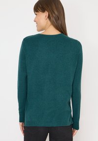 Suéter de manga larga en color teal con cuello redondo. Textura suave y puños acanalados. Dobladillo trasero ligeramente más largo con aberturas laterales para mayor libertad de movimiento.