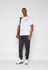 Witte t-shirt met korte mouwen en zwart Puma-logo, gecombineerd met donkergrijze sweatpants en witte sneakers. Eenvoudig, sportief ontwerp.