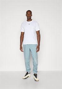Hvit T-skjorte med kort erm og svart Jordan-logo; lyseblå joggebukser med mønstrede detaljer; svart og hvit sneakers.
