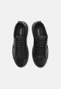 Baskets noires avec une tige en cuir texturé, des lacets ronds, et une semelle en caoutchouc épaisse distinctive avec des accents rainurés.