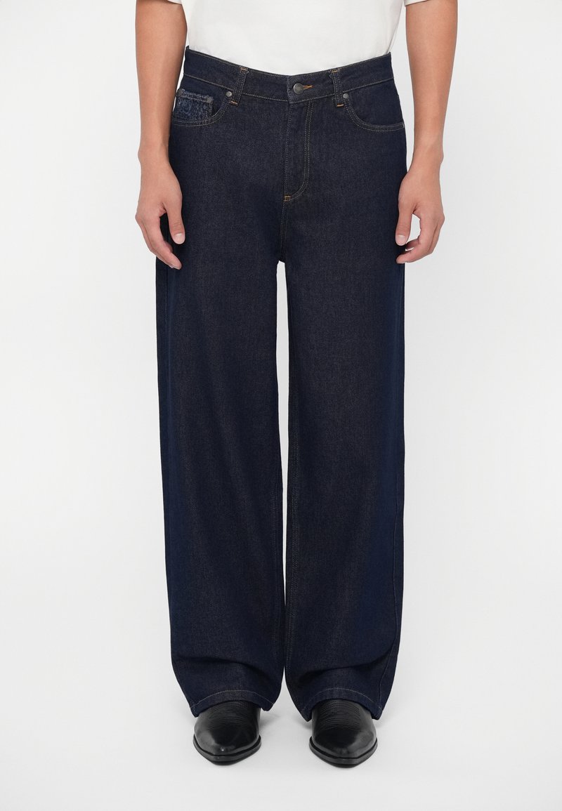 Vaqueros de pierna ancha de color azul oscuro, confeccionados en denim con una cintura alta, que presentan costuras en contraste, bolsillos frontales y un cierre de botón.