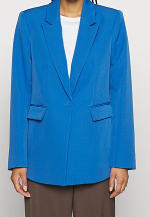 Blue blazer with a notched collar, single button closure, two front pockets, tailored fit, and smooth texture. Worn over a white top.