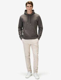 Grå hoodie med en framficka, dragsko på huvan och ribbade ärmslut, kombinerad med ljusa byxor och vita sneakers.