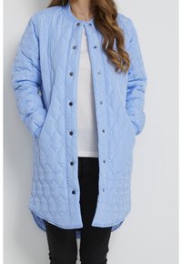 Tikkitakki sinisessä värissä, pyöreällä kauluksella, edessä painonapeilla suljettava, sivutaskuilla ja hieman pidemmällä takareunalla. Pehmeä, sileäpintainen materiaali.