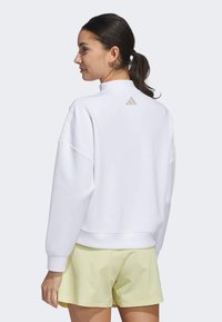 White sweatshirt with a high collar and oversized fit, featuring a subtle beige logo on the back; paired with light yellow textured shorts.