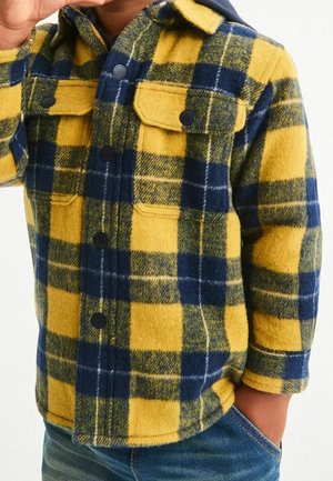 Gul och marinblå rutigt flaneljacka med knappstängning fram, två bröstfickor och krage. Mjuk textur; något överdimensionerad passform.