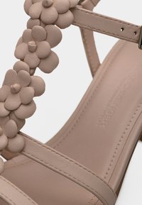 Ροζ δερμάτινο σανδάλι με διακοσμητικά σε σχήμα λουλουδιού, επίπεδη σόλα και λεπτά λουράκια. Ομαλή υφή και ελάχιστα ραφές.