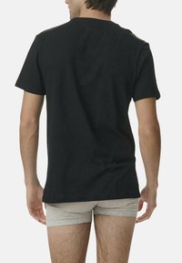 T-shirt en coton noir à manches courtes, col rond et coupe décontractée, vue de dos. Porté avec un short gris.