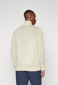 Cream turtleneck sweater made of soft knit fabric, featuring a fitted design and ribbed cuffs, shown from the back against a plain background.