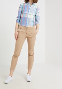Camicia a quadri blu, rosa e verde; abbinata a pantaloni beige aderenti e scarpe da ginnastica bianche, che mostrano un abbigliamento casual.