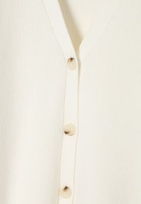 Cream-colored ribbed cardigan with a v-neckline and five round beige buttons on the front. Soft texture and lightweight design.