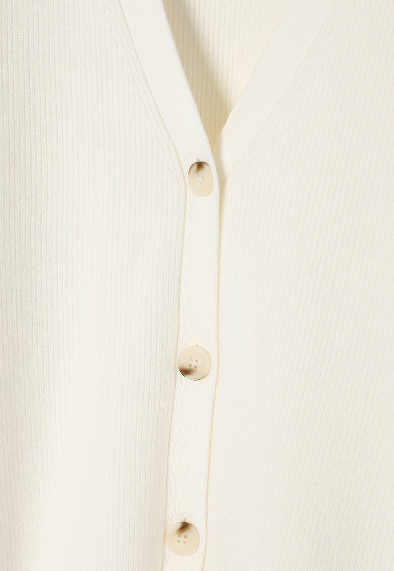 Kardigan w kolorze kremowym, prążkowany, z dekoltem w serek i pięcioma okrągłymi beżowymi guzikami z przodu. Miękka tekstura i lekka konstrukcja.