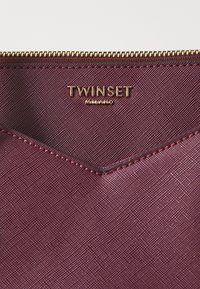 Burgundy fabric zip pouch featuring a gold-tone "TWIXSET" logo, stitched edges, and a textured surface with a chevron design.