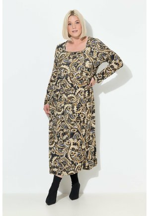 Robe longue noire avec un motif paisley doré complexe, col rond et manches longues, associée à des bottines noires à la cheville.