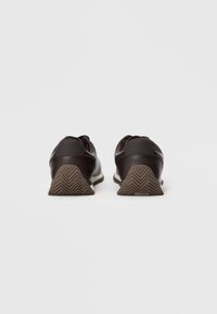Zapatillas deportivas marrones con un acabado de cuero texturizado, que presentan una suela de goma resistente con un patrón en zigzag y acentos en contraste.