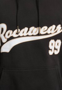 Fekete kapucnis pulóver állítható zsinórral, fehér és arany hímzett "Rocawear" felirattal és "99" részlettel az elején. Tartós anyag textúra.
