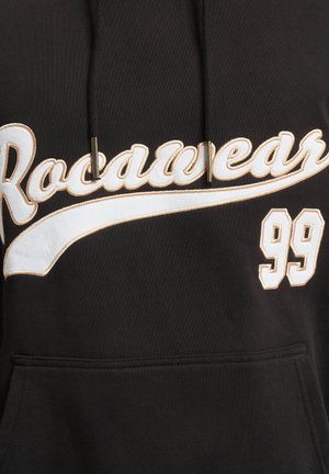 Svart hettegenser med snor, med hvit og gull brodert "Rocawear"-tekst og "99" detalj på forsiden. Slitesterk stoffkvalitet.