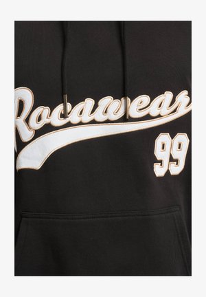 Svart hettegenser med snor, med hvit og gull brodert "Rocawear"-tekst og "99" detalj på forsiden. Slitesterk stoffkvalitet.