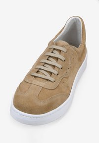Zapatilla de ante beige con punta redonda, cordones planos y suela de goma blanca. Presenta detalles de costura en la parte superior y perforaciones para transpirabilidad.