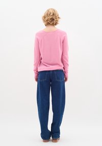 Różowy, dziergany sweter z długimi rękawami, okrągłym dekoltem i prążkowanym obrzeżem, zestawiony z szerokimi niebieskimi dżinsami z tylnymi kieszeniami.